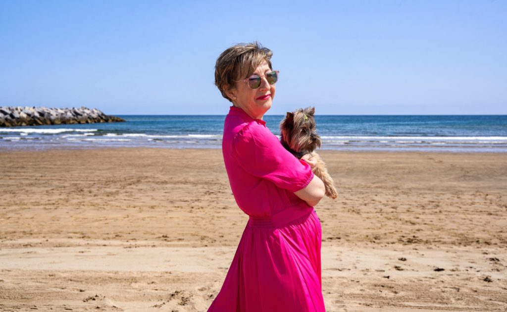 Mujer con vestido rosa y perro Yorkshire en brazos en la playa